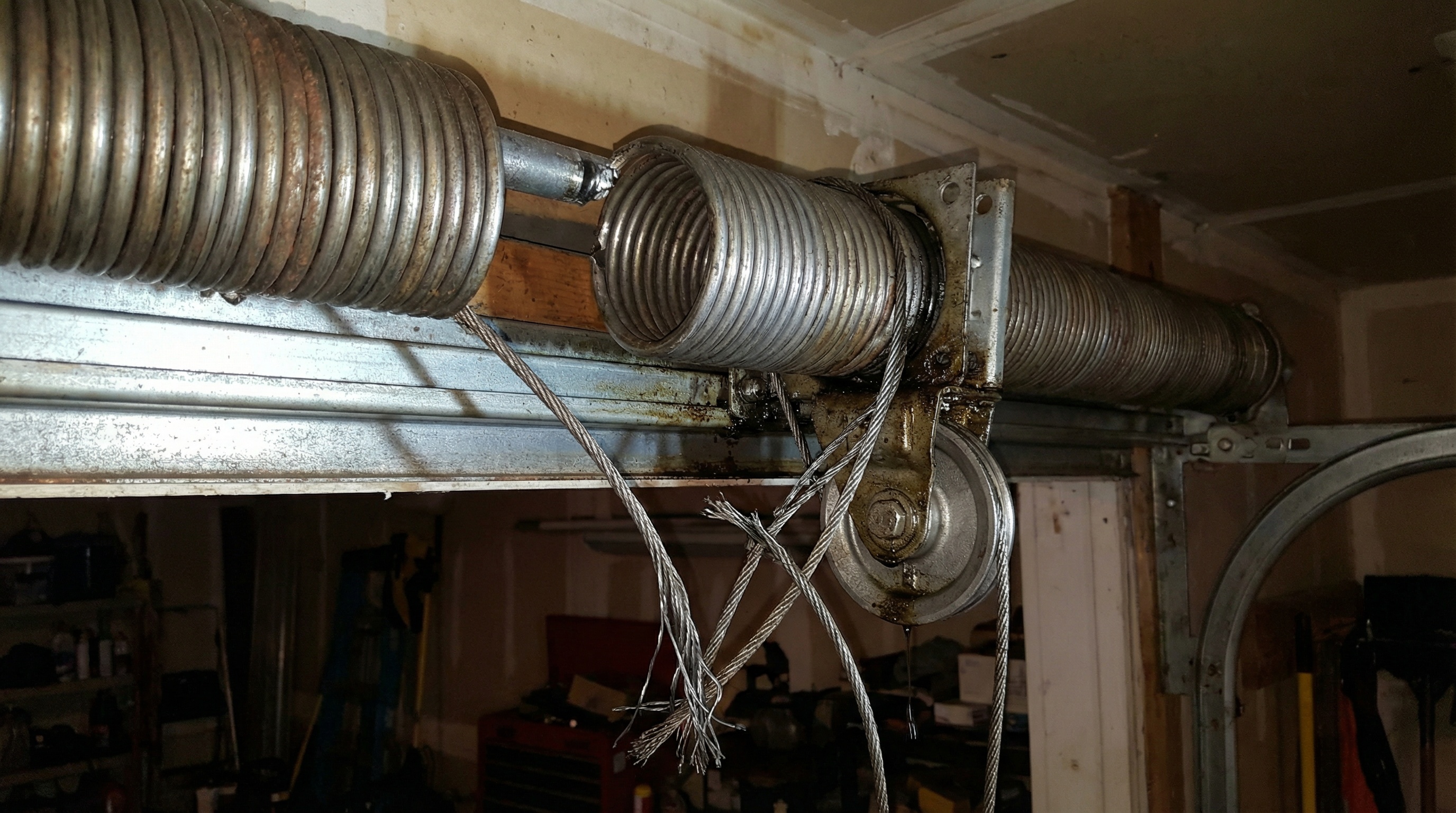 Broken garage door spring with visible gap and frayed cables showing safety hazard