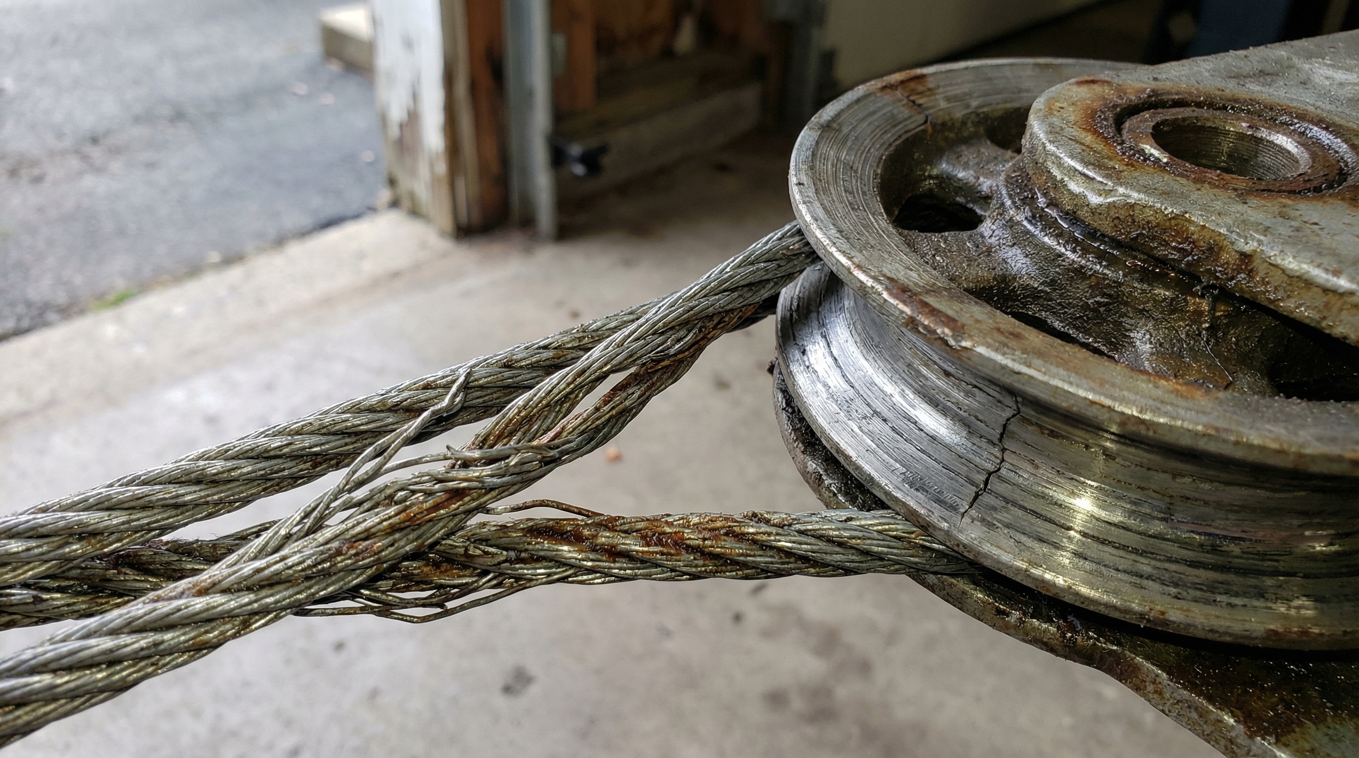Close-up view of frayed garage door cables and worn pulleys showing signs of failure