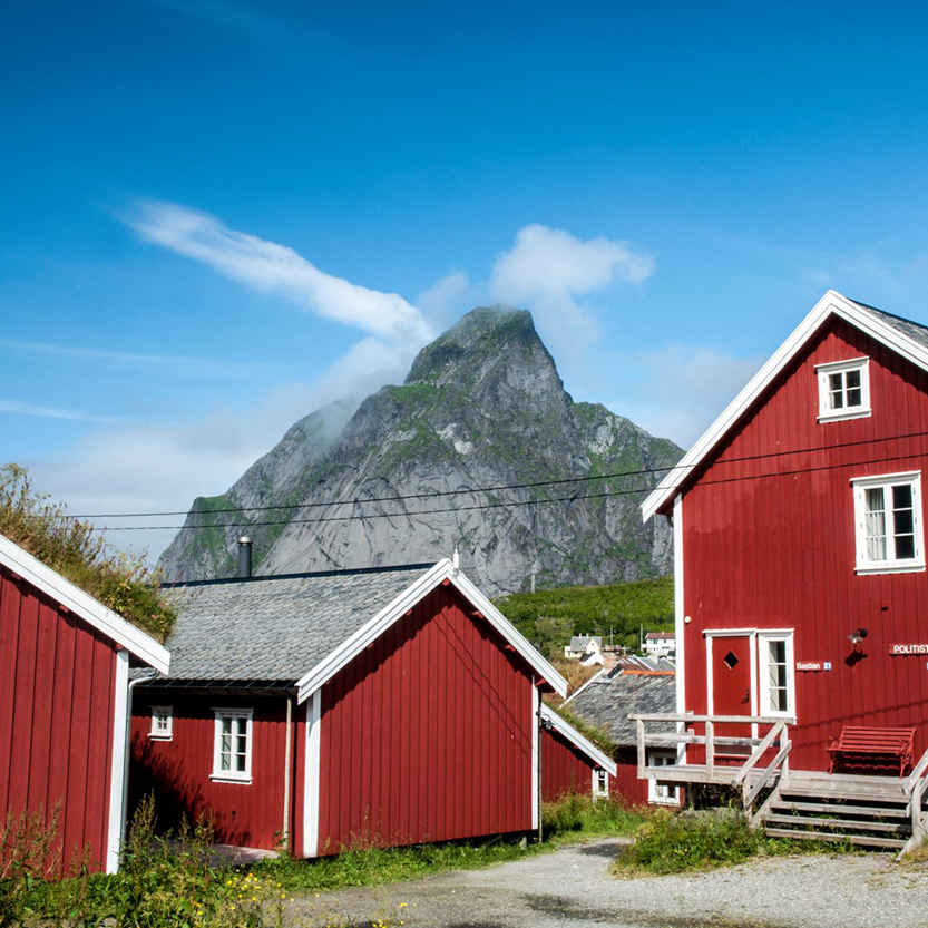 een foto van rode huisjes in noorwegen met een bergtop op de achtergrond