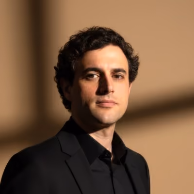 Portrait of Evan wearing a black blazer against a warm background.
