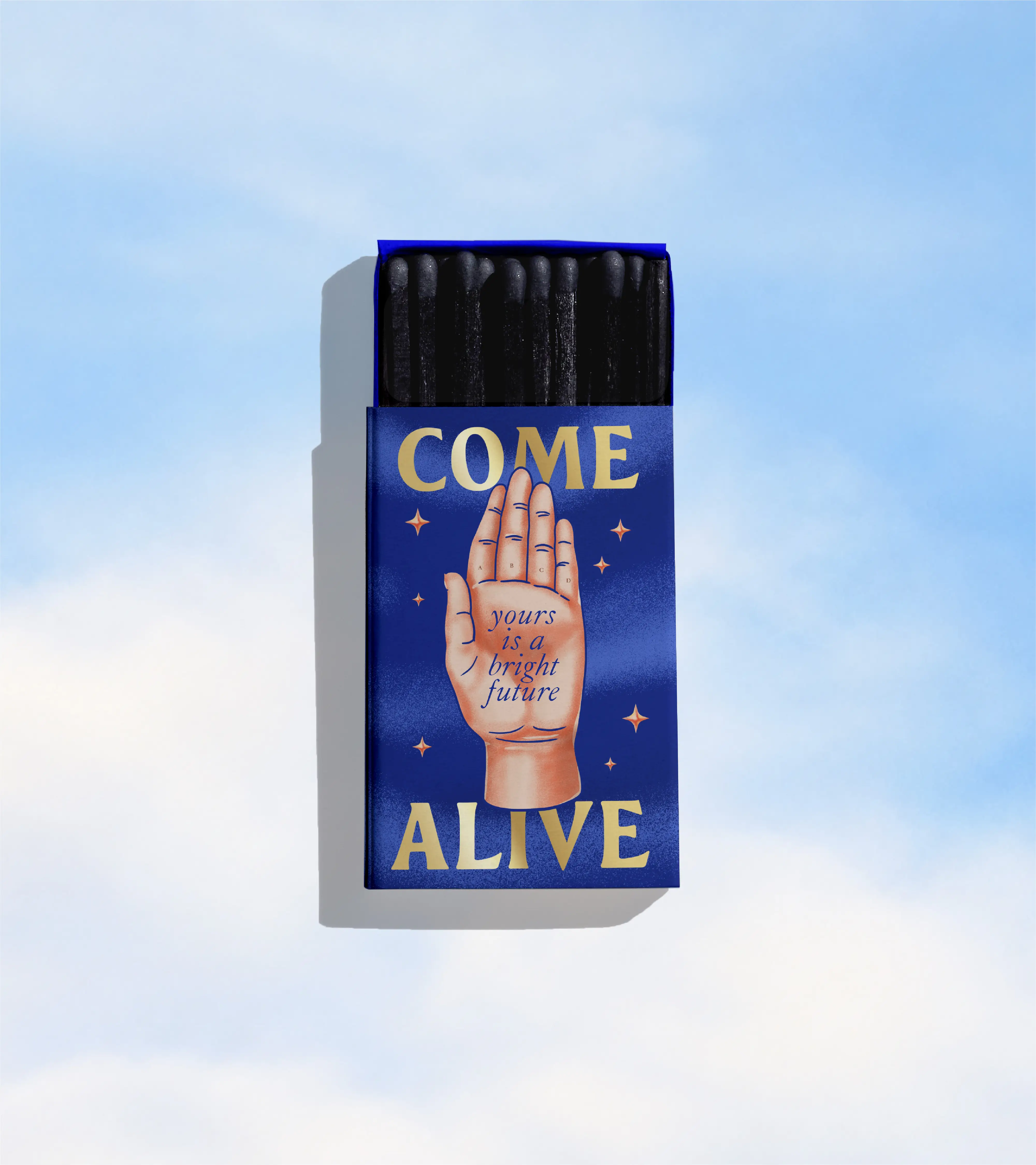 An open matchbox shown on a blue cloud background. The design on the matchbox says "come alive" with a palm reading diagram on it. In the middle of the palm it says "yours is a bright future"