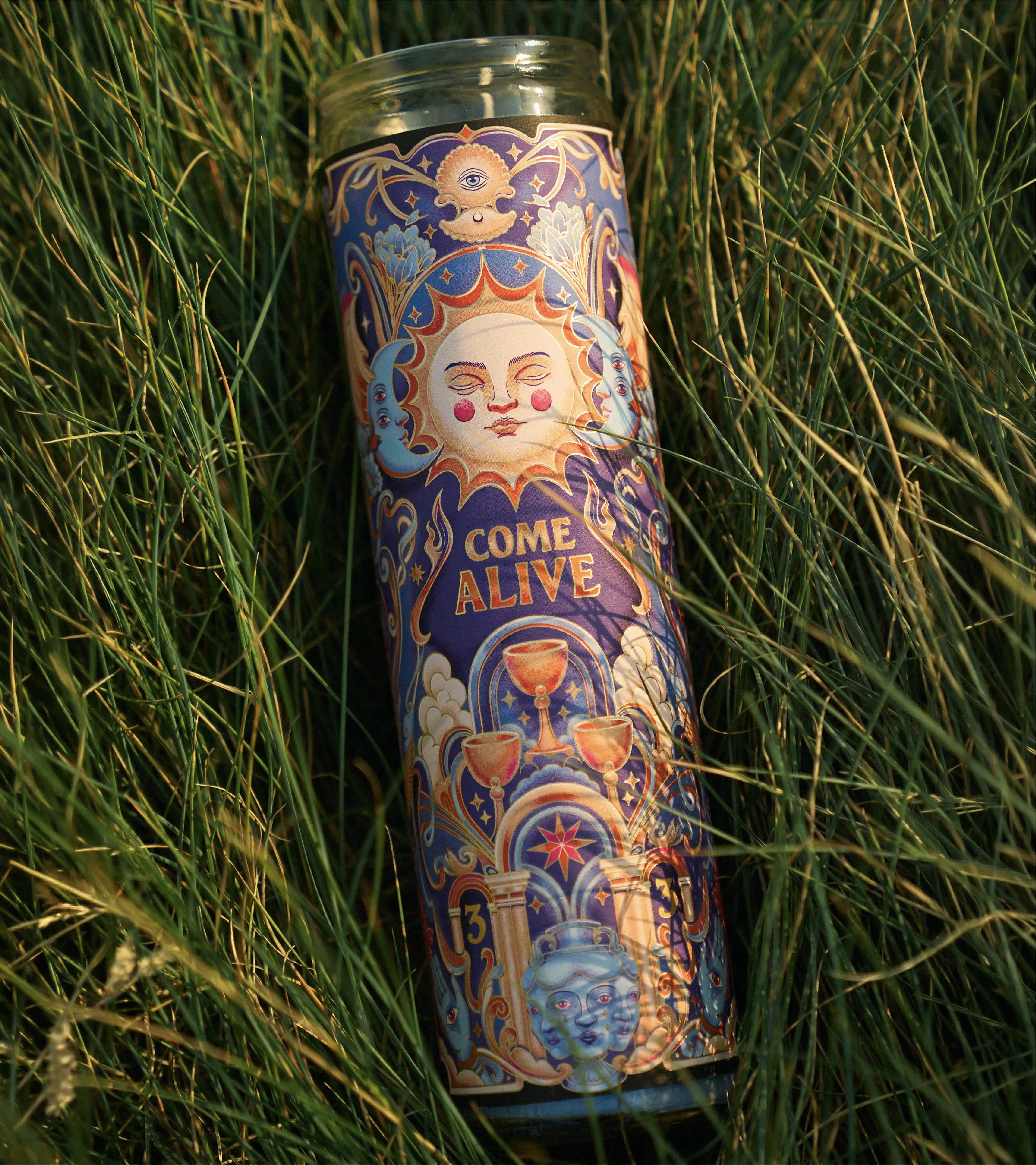 Close up image of the candle design nestled in a patch of green grass as sunset