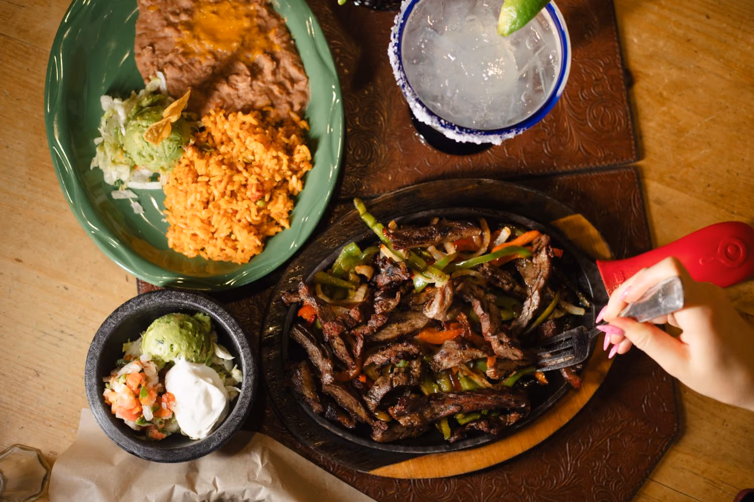 Table with pan of fajitas, various sides and a margarita
