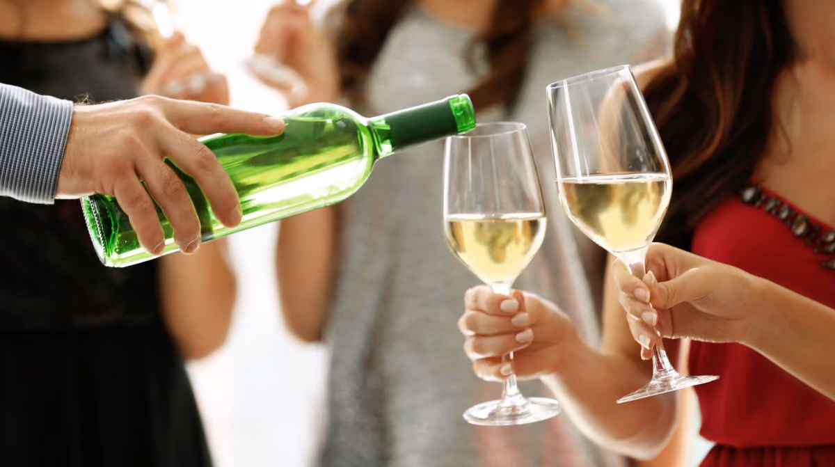 Man pouring white wine in glasses two women are holding