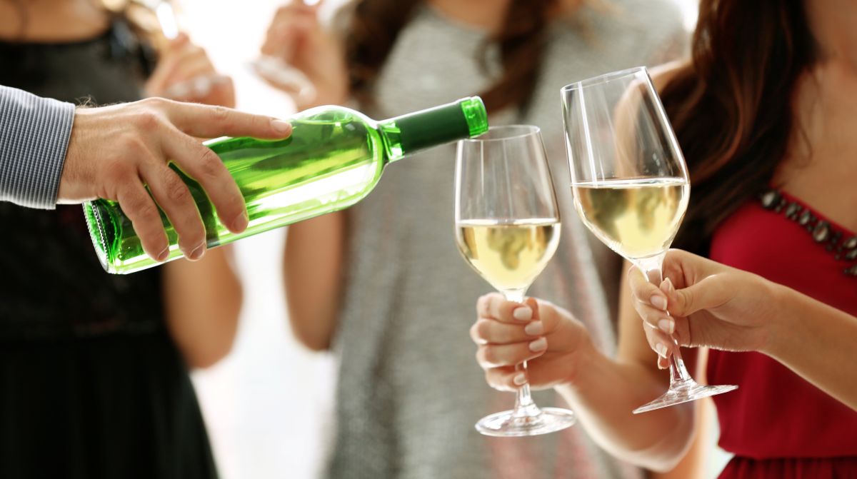 Man pouring white wine in glasses two women are holding