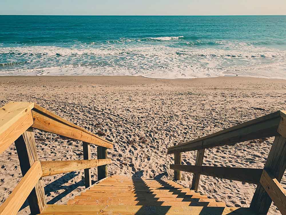 Wooden stairs leading down to a sandy beach and ocean waves.