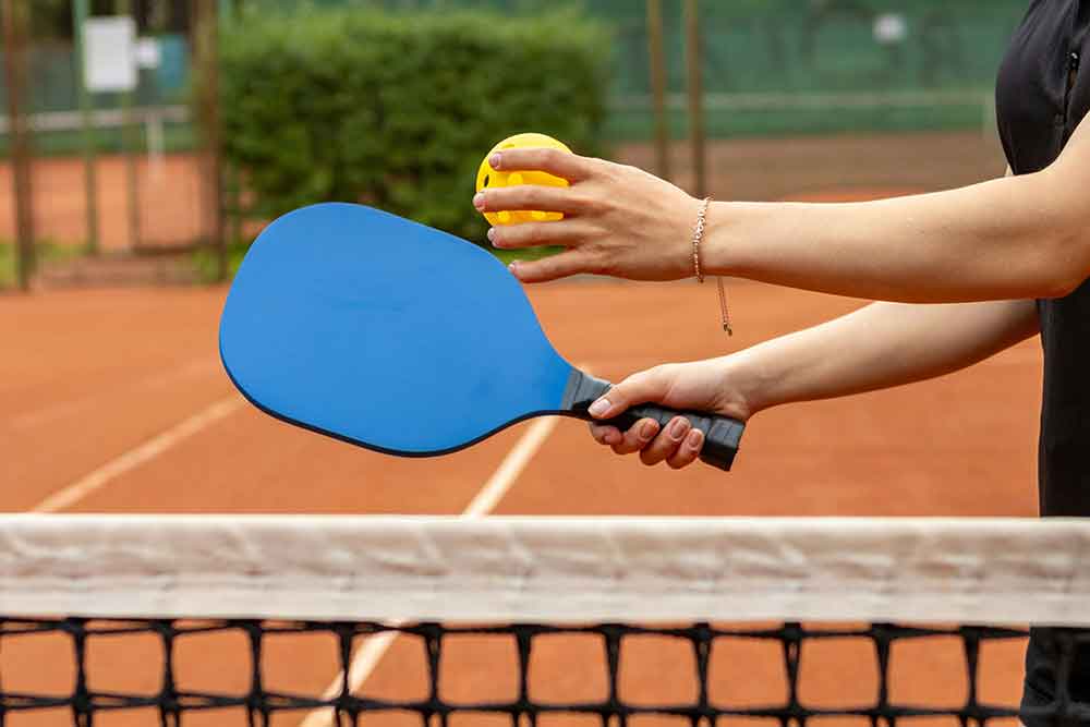 Person holding a paddle and ball on a clay pickleball court.