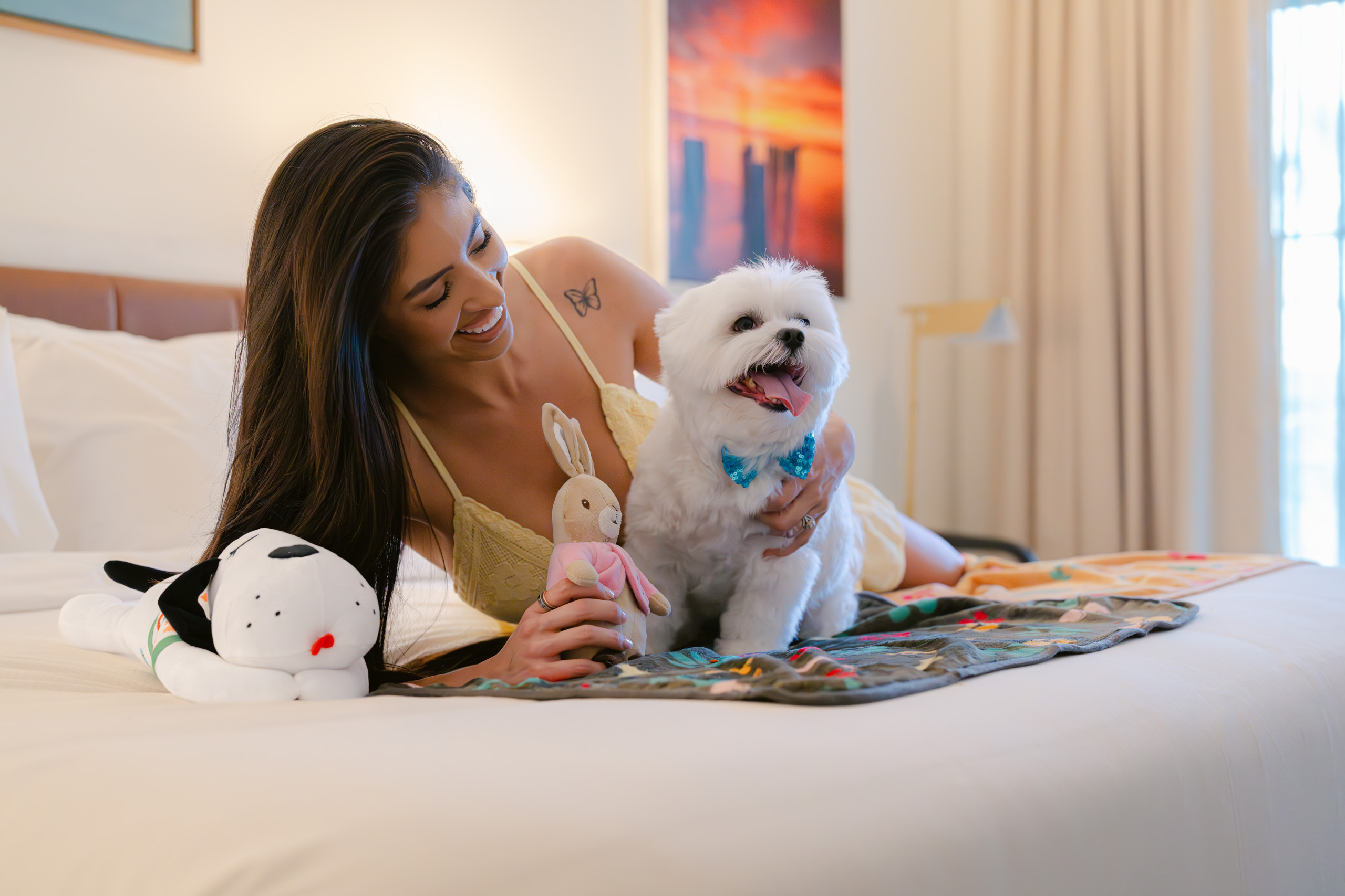 Woman smiling and cuddling small white dog on hotel bed