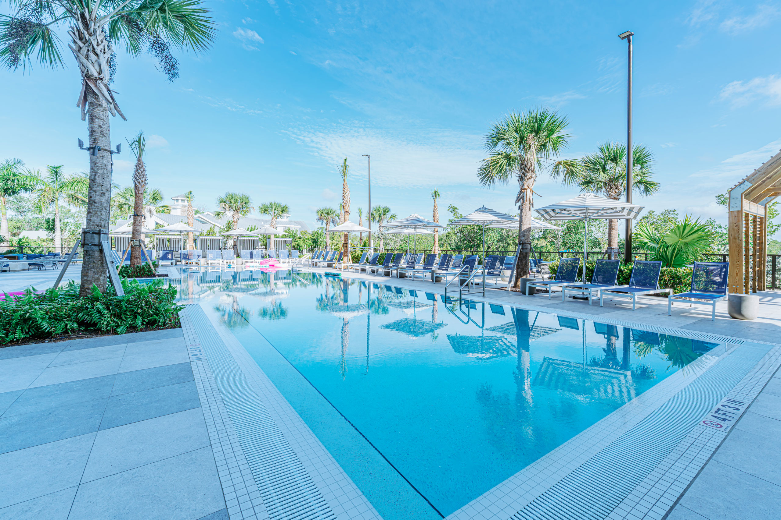 Outdoor swimming pool lined with lounge chairs, umbrellas, and palm trees.