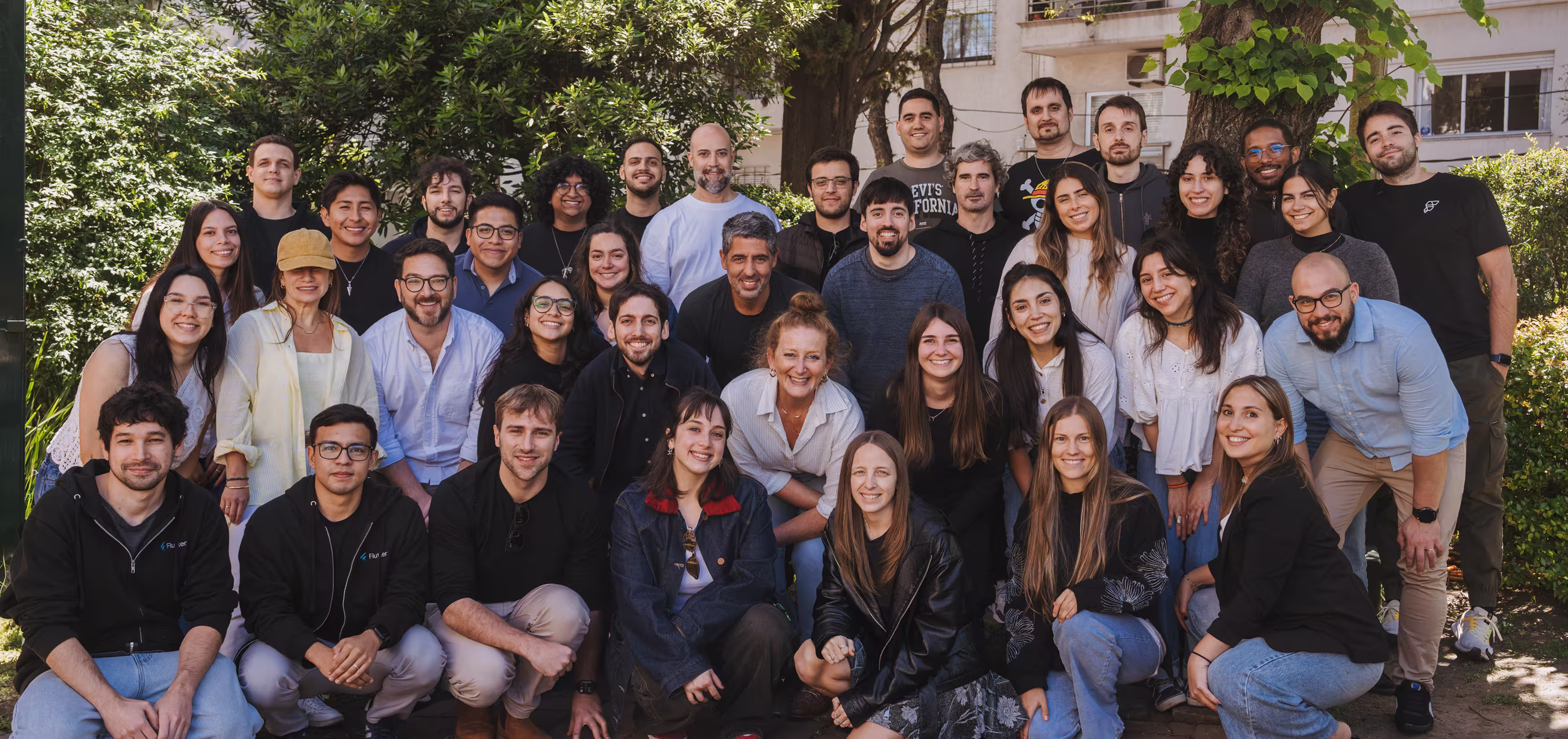 Group photo of around 35 diverse people outdoors in a garden, smiling and posing together.