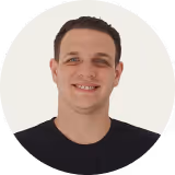 Smiling man with short dark hair wearing a black shirt against a white background.