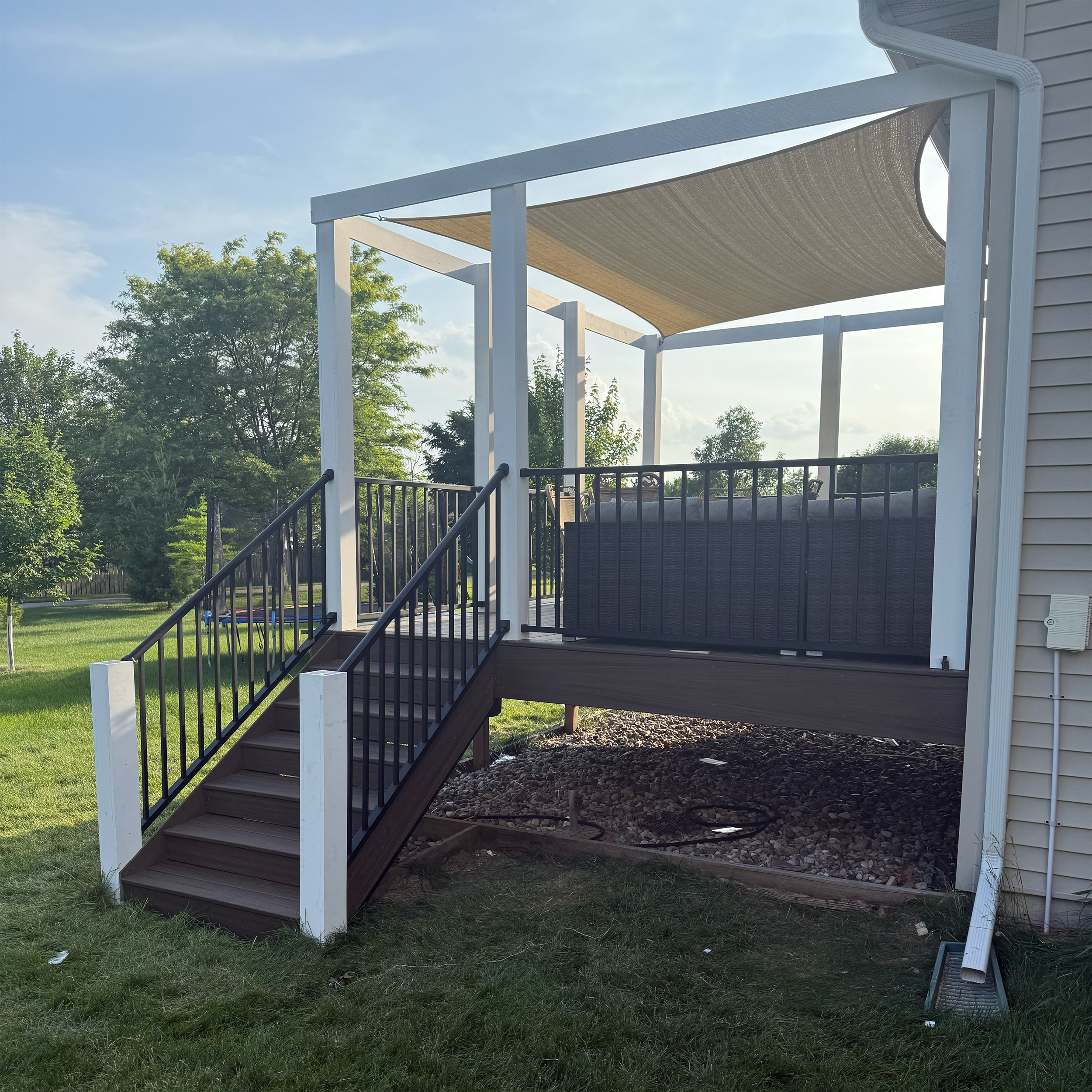 Wooden backyard deck with black railing and a beige shade sail attached to a house.