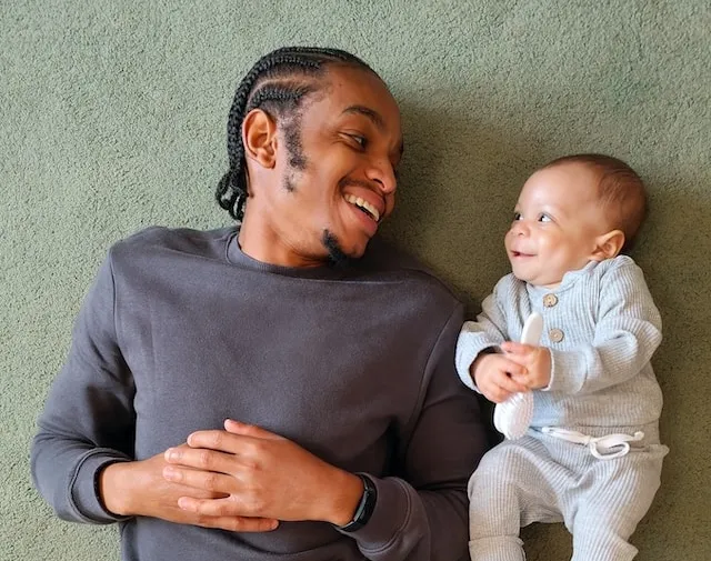 A man laying on the floor looking and smiling at his newborn baby beside him