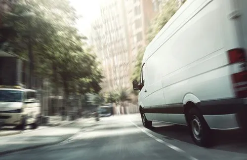 A shipping cargo van driving down a less than busy metropolitan street