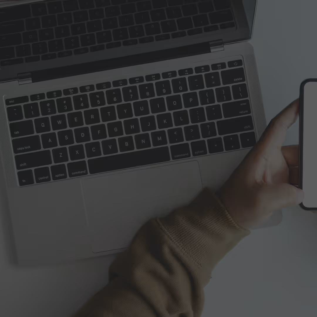 a person holding a phone and using a laptop
