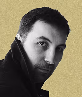 Black and white portrait of a man with short hair wearing a dark coat, looking at the camera.