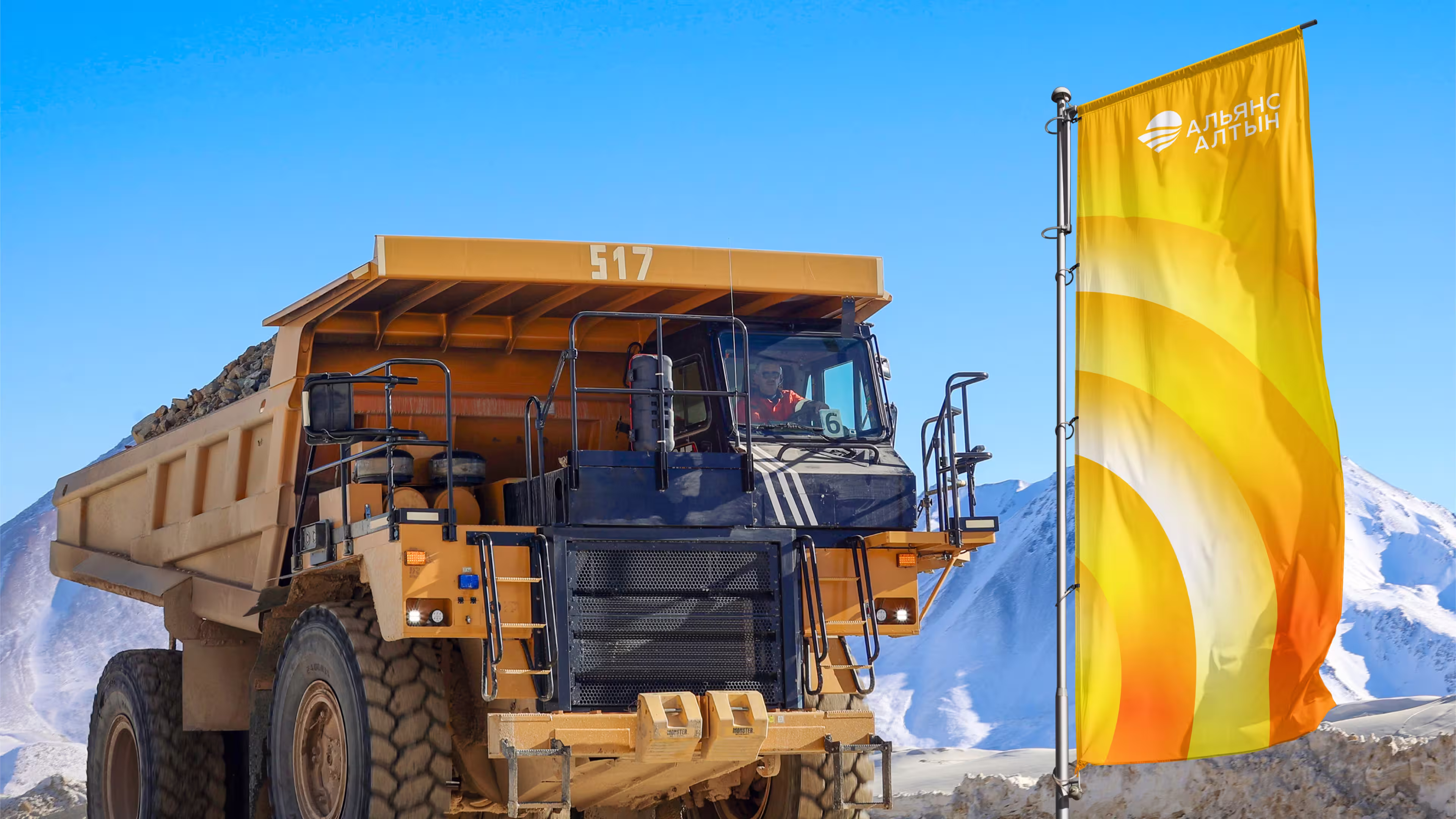Large mining dump truck loaded with rocks near a yellow flag with Cyrillic text in snowy mountains.