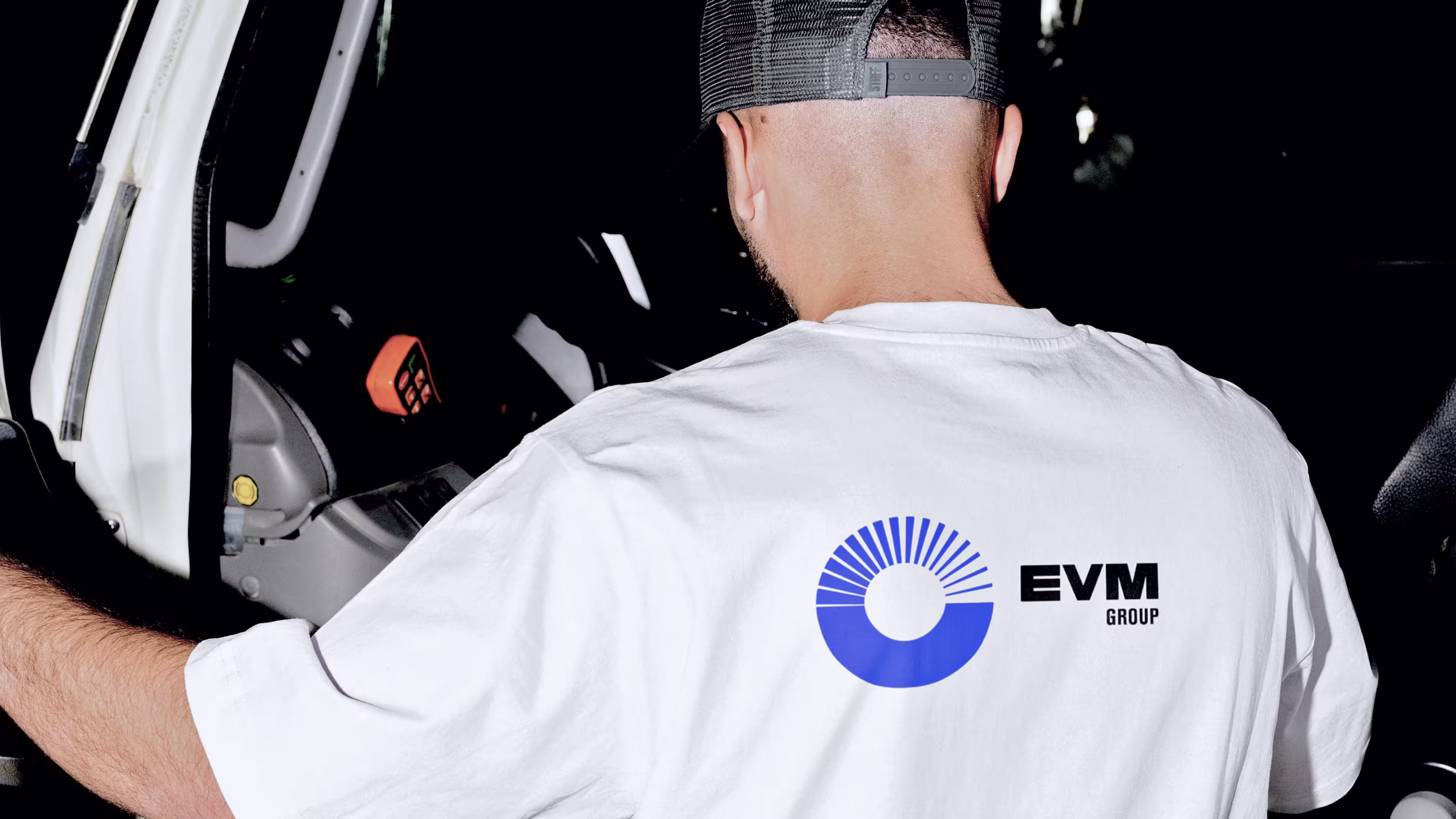 Man wearing a white shirt with a blue circular logo and EVM Group text on the back.