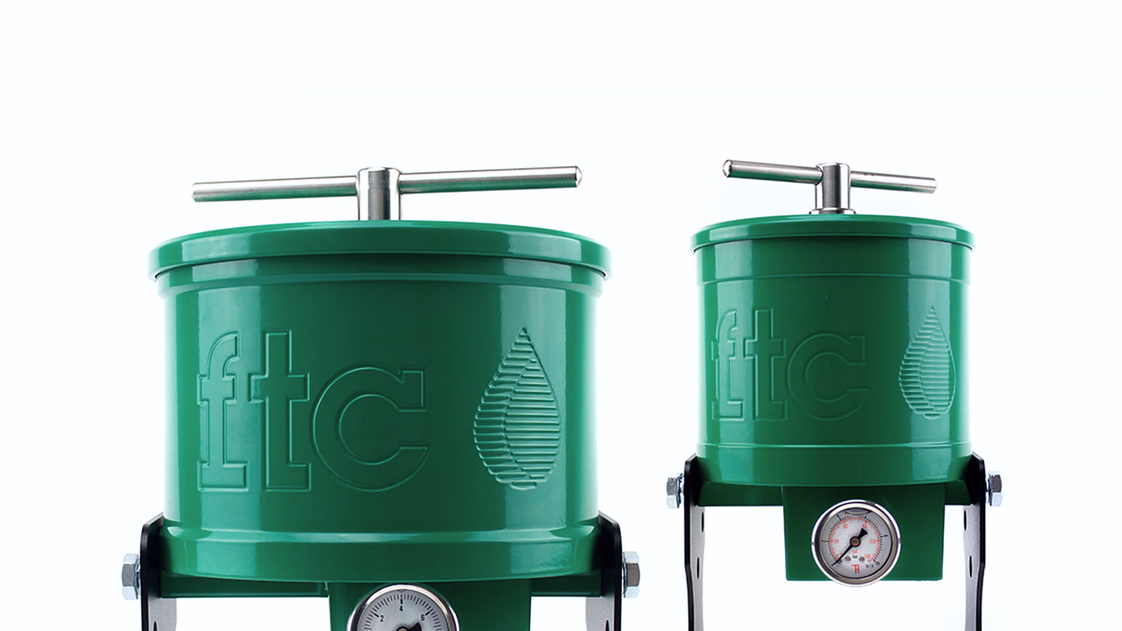 Two green cylindrical filters with FTC branding and pressure gauges on metal brackets.