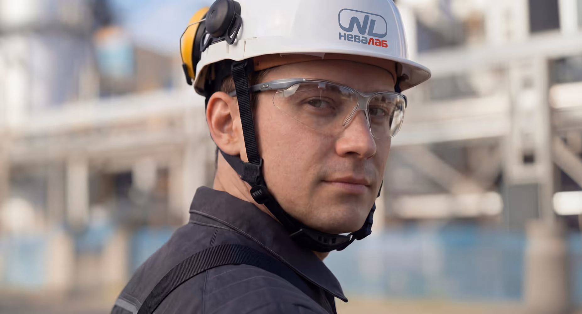 Man wearing a white hard hat and safety glasses at an industrial site.