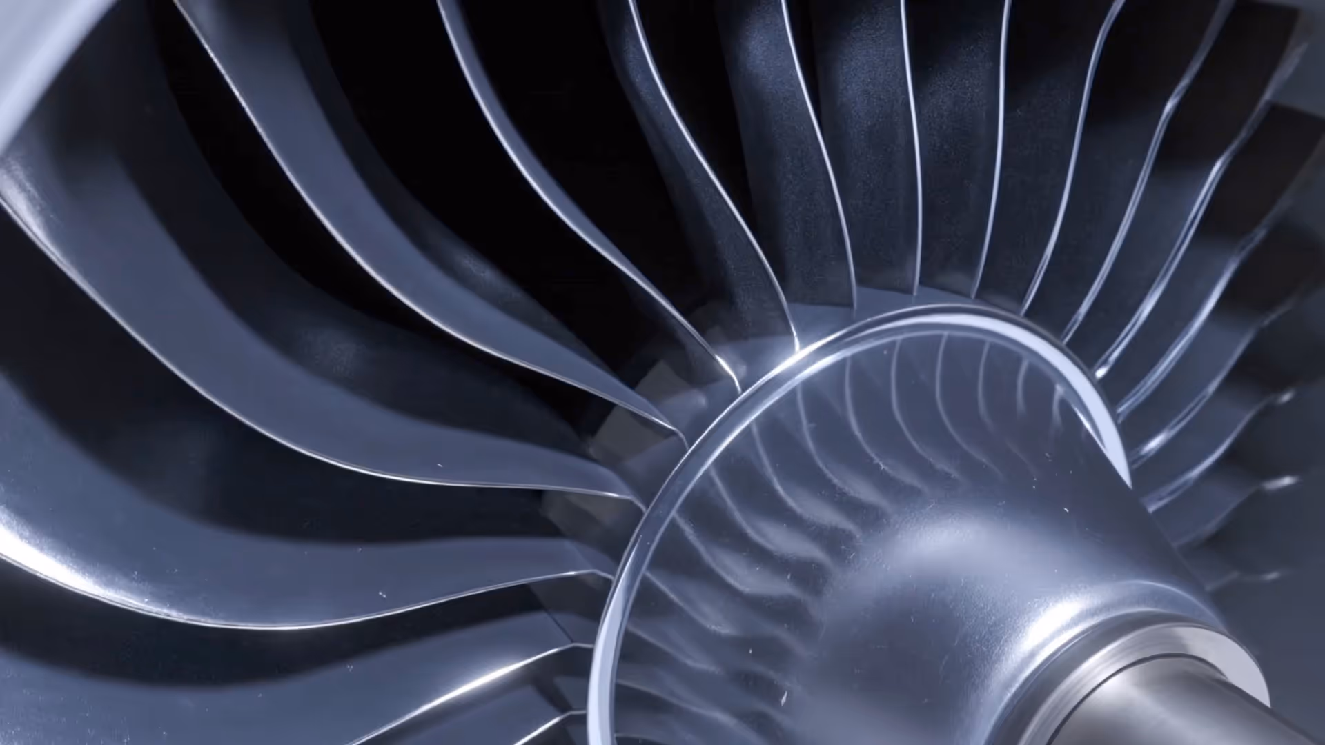 Close-up of a metallic turbine engine fan with curved blades and reflective surfaces.
