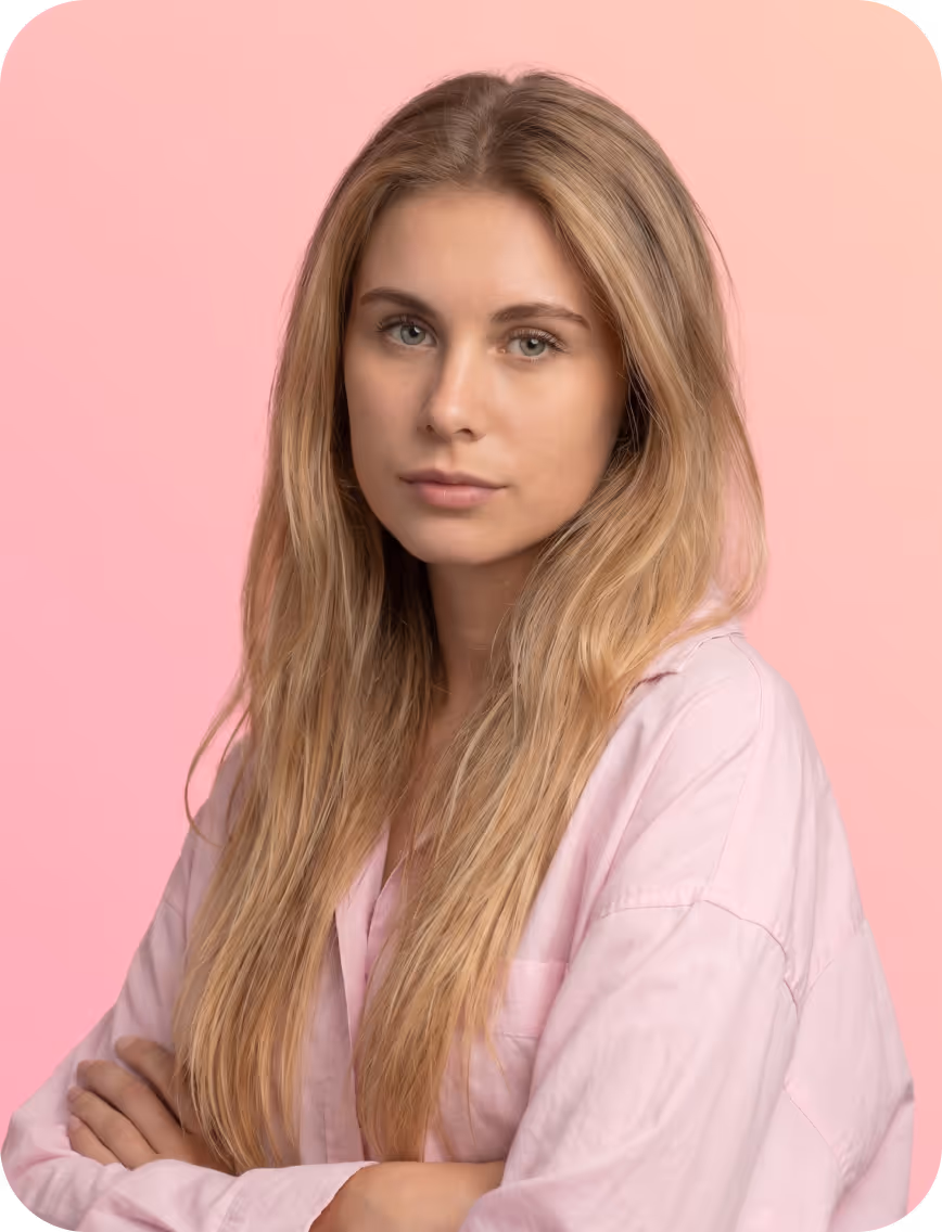 Young woman with long blonde hair in a light pink shirt against a pink background, arms crossed.