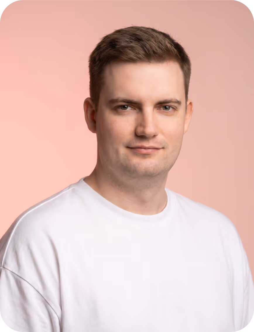 Young man with short brown hair wearing a white shirt against a pink background.