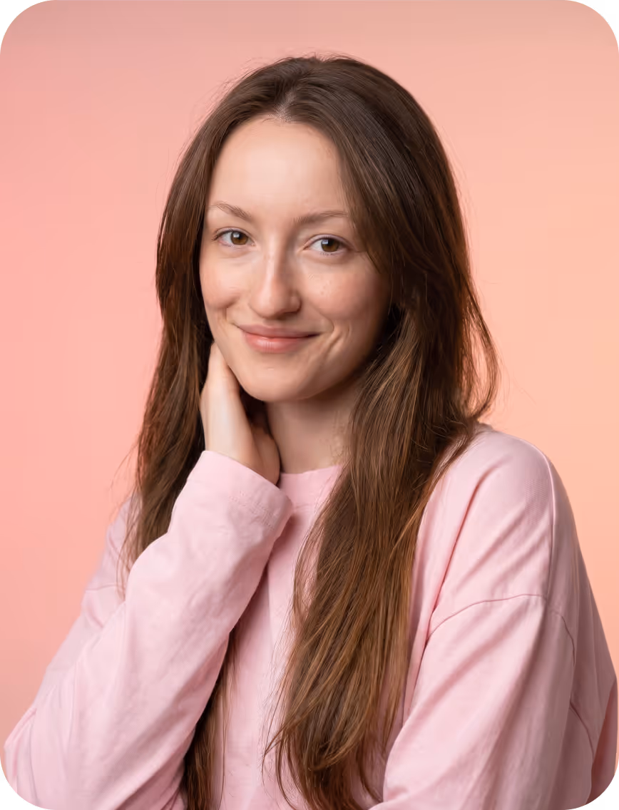 Smiling woman with long brown hair wearing a pink sweater against a soft peach background.