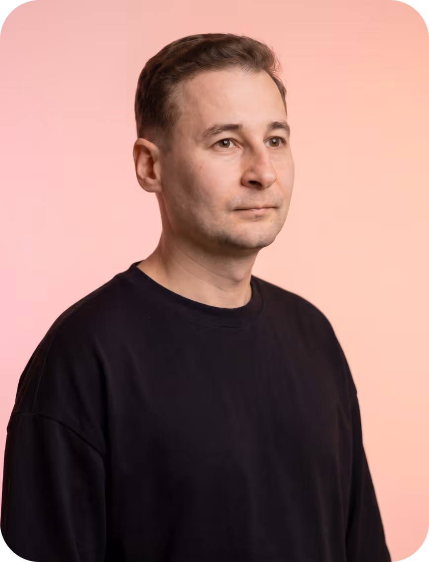 Man with short brown hair wearing a black shirt against a pink gradient background.