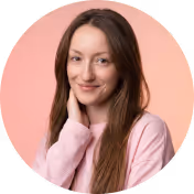 Smiling woman with long brown hair in a pink sweater against a soft pink background.