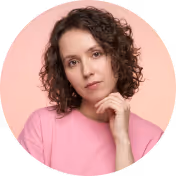 Portrait of a woman with curly hair wearing a pink top, resting chin on her hand.