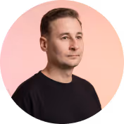 Portrait of a man with short brown hair wearing a black shirt against a pink background.