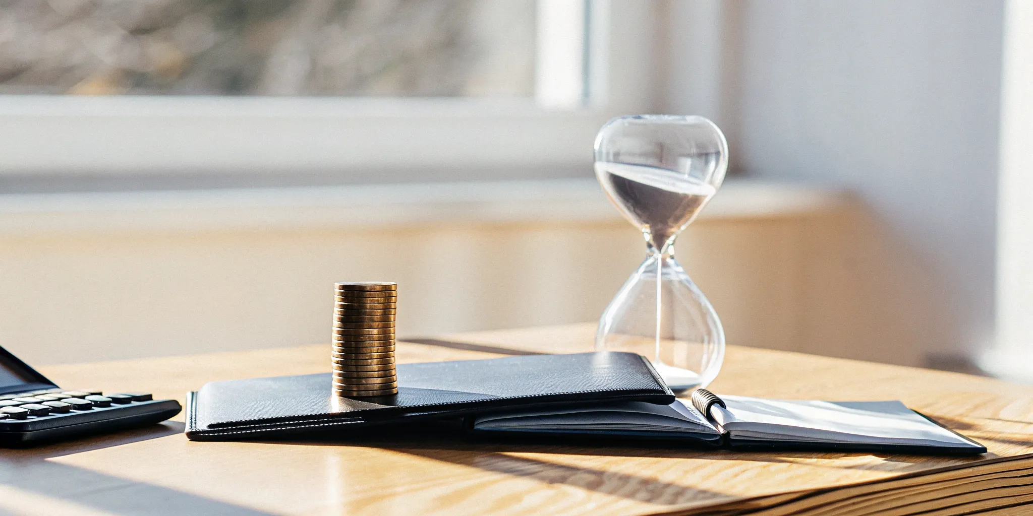 An hourglass and stack of coins on a ledger comparing accrued revenue vs deferred revenue.