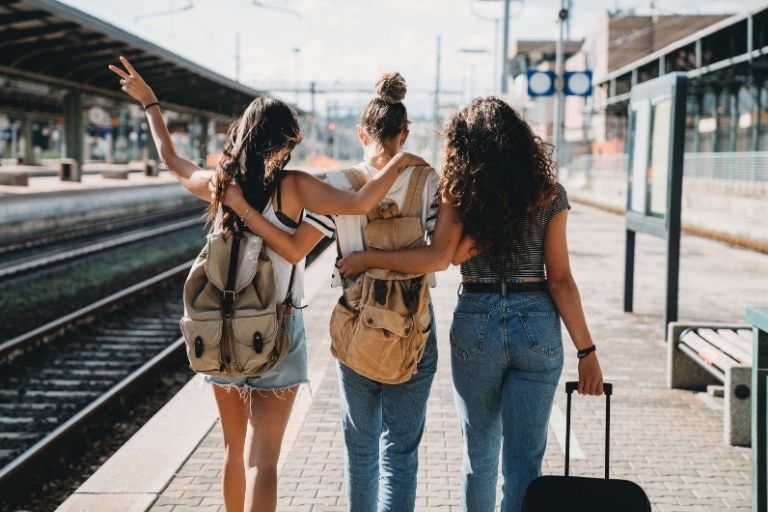 Drie jonge vrouwen op perron met tassen en koffer