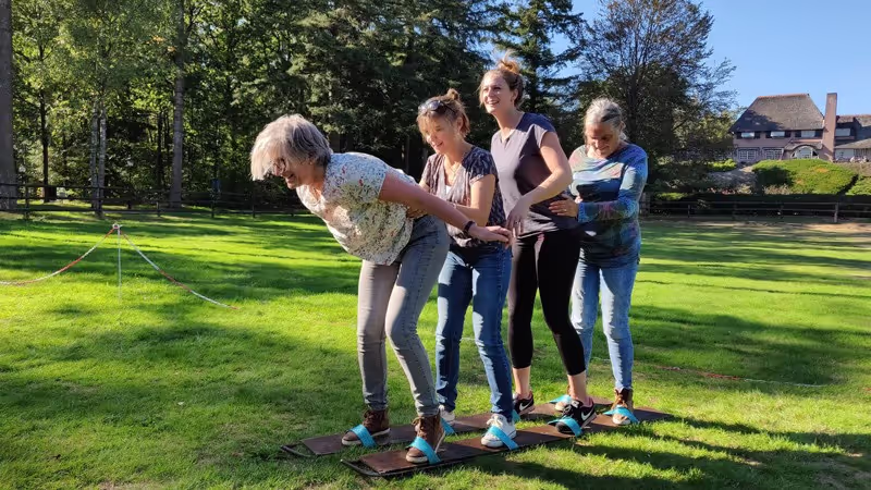 vier vrouwen proberen te lopen op grote loopski's op een grasveld