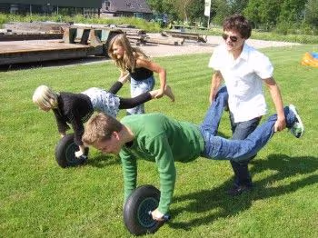 mensen bootsen een kruiwagen na als onderdeel van een zeskamp