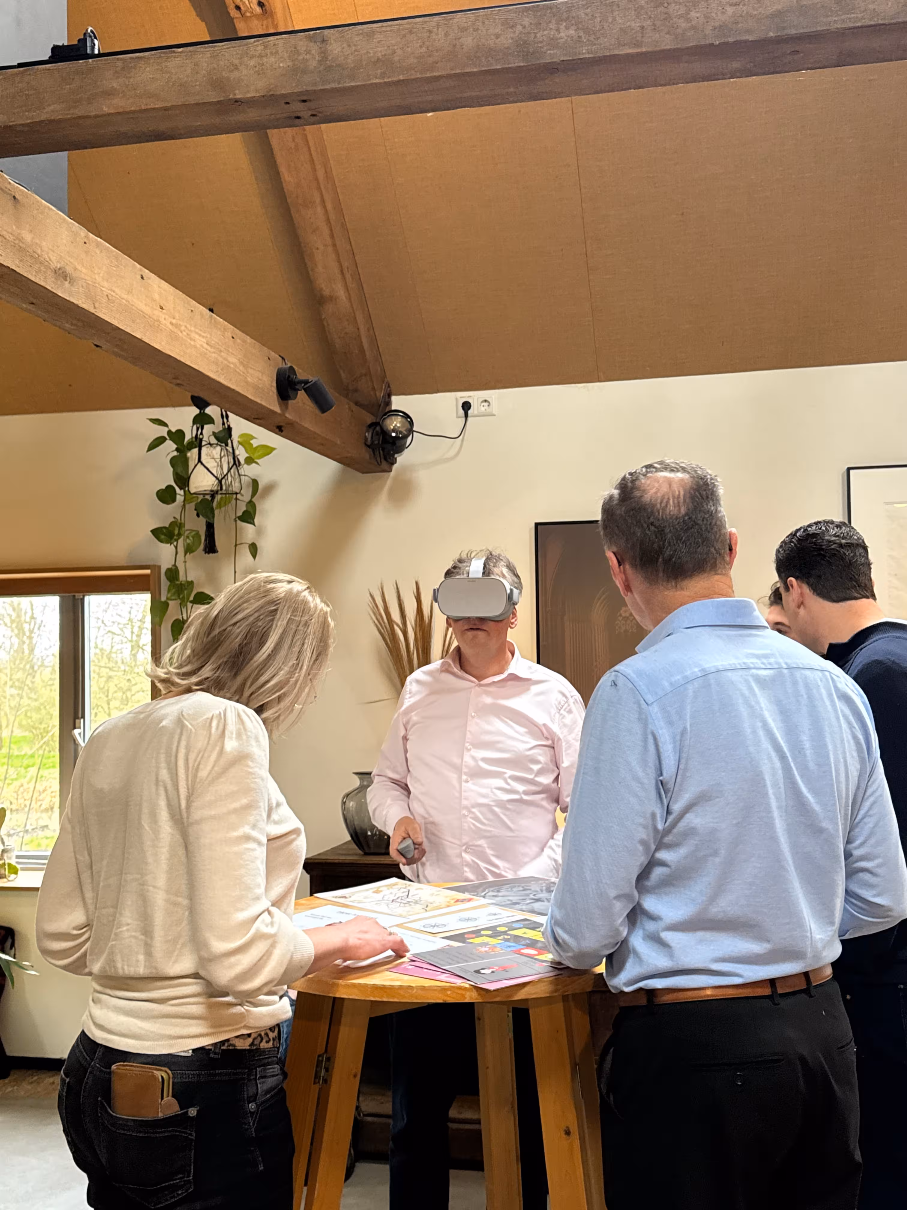 Een man draagt een VR bril en het team staat rondom een houten statafel tijdens het moordspel