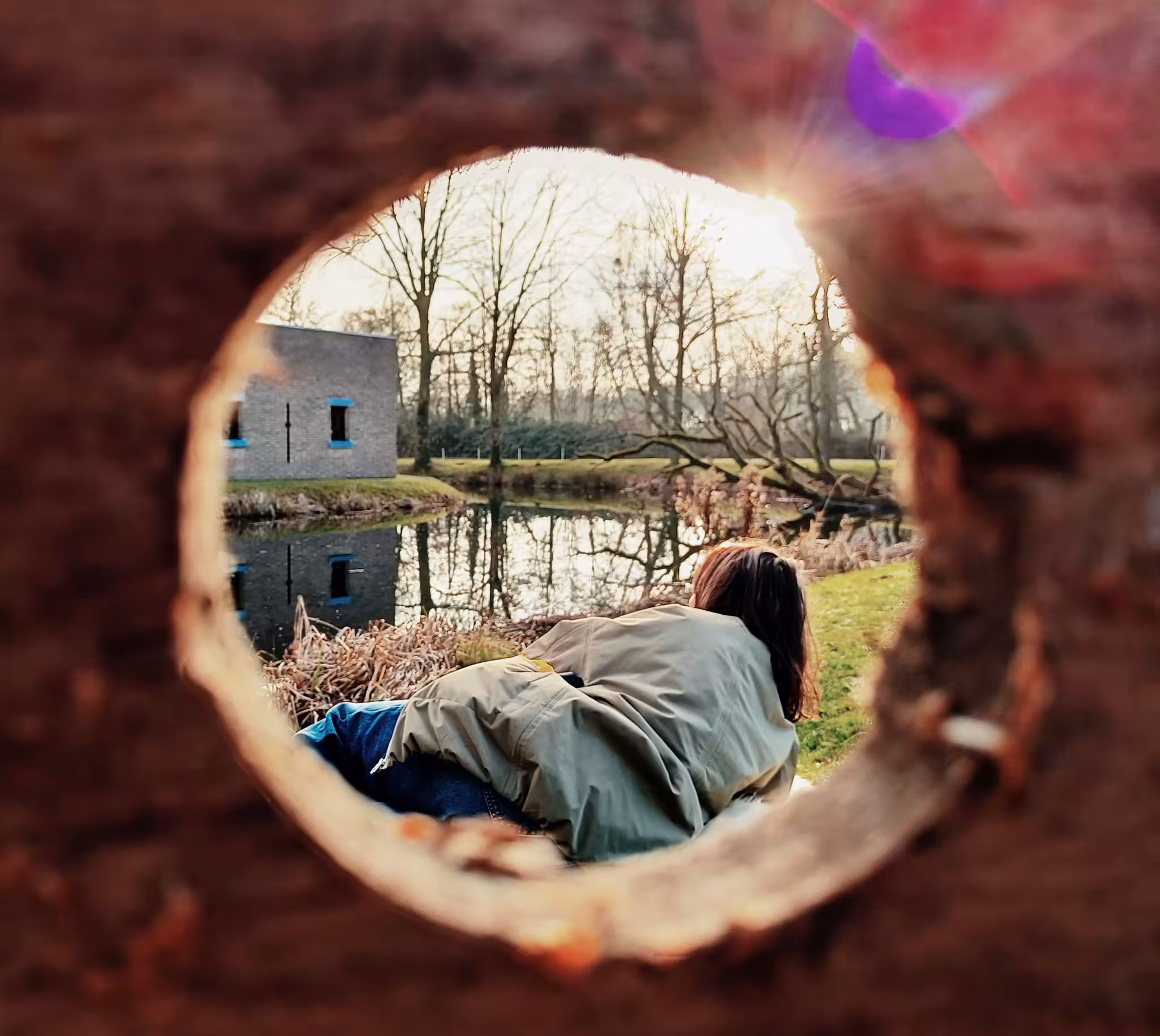 Een vrouw ligt in het gras en kijkt richting een gebouw omringd door water