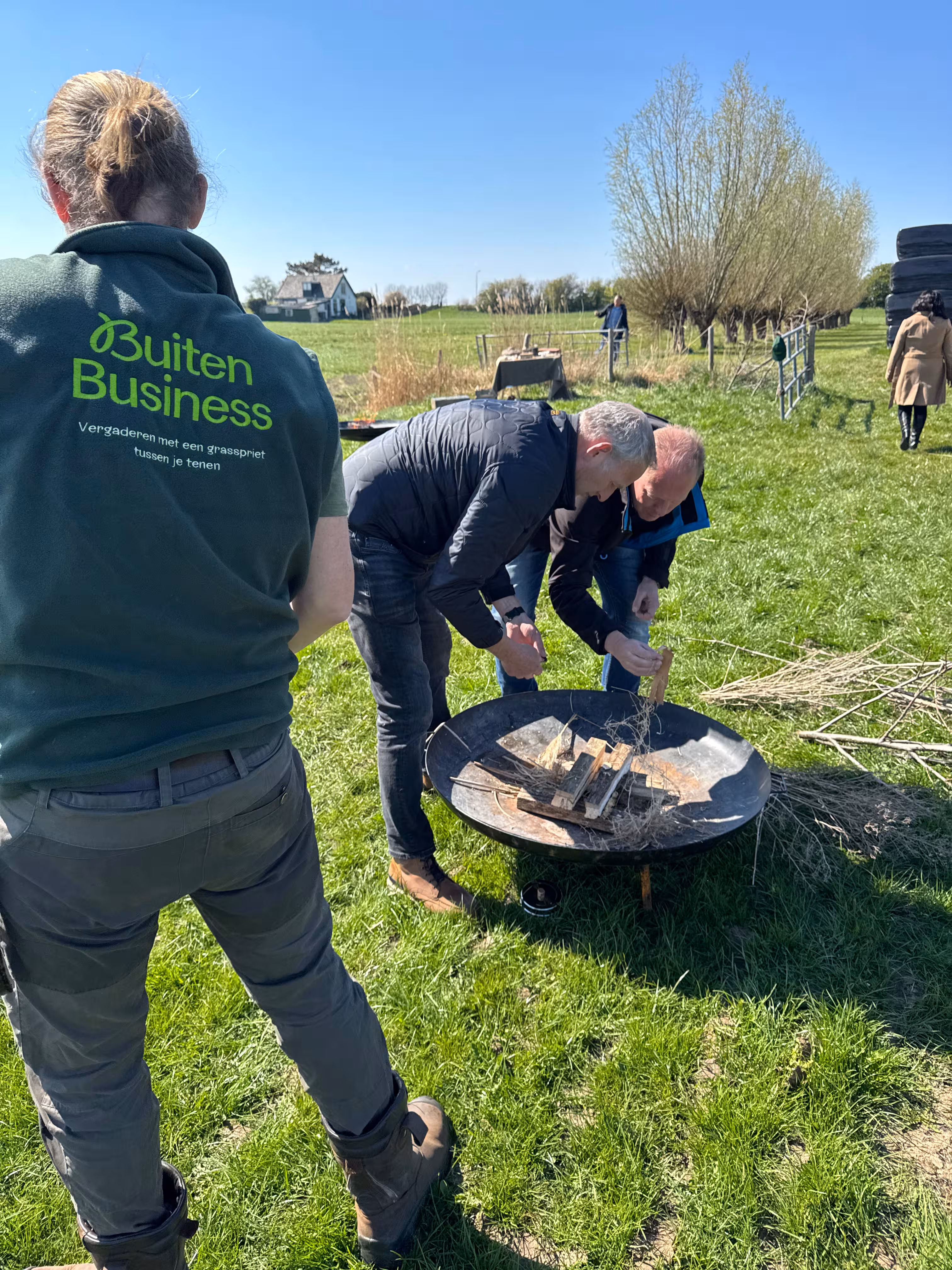 De BuitenEvents instructeur kijkt naar twee personen die in een vuurschaal proberen vuur te maken