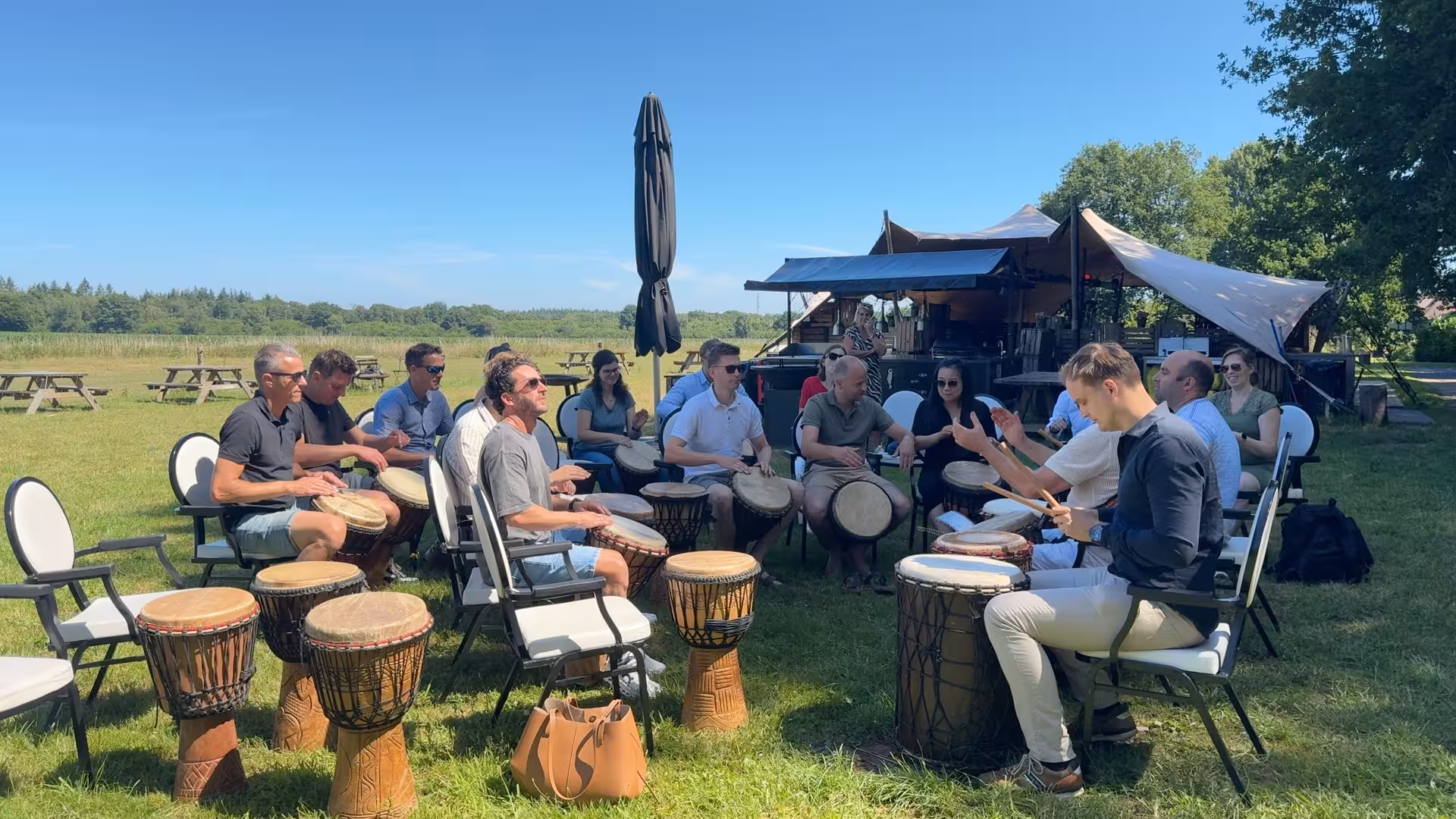 Er wordt op een grasveld een percussie workshop verzorgd door BuitenEvents tijdens een zomerse dag
