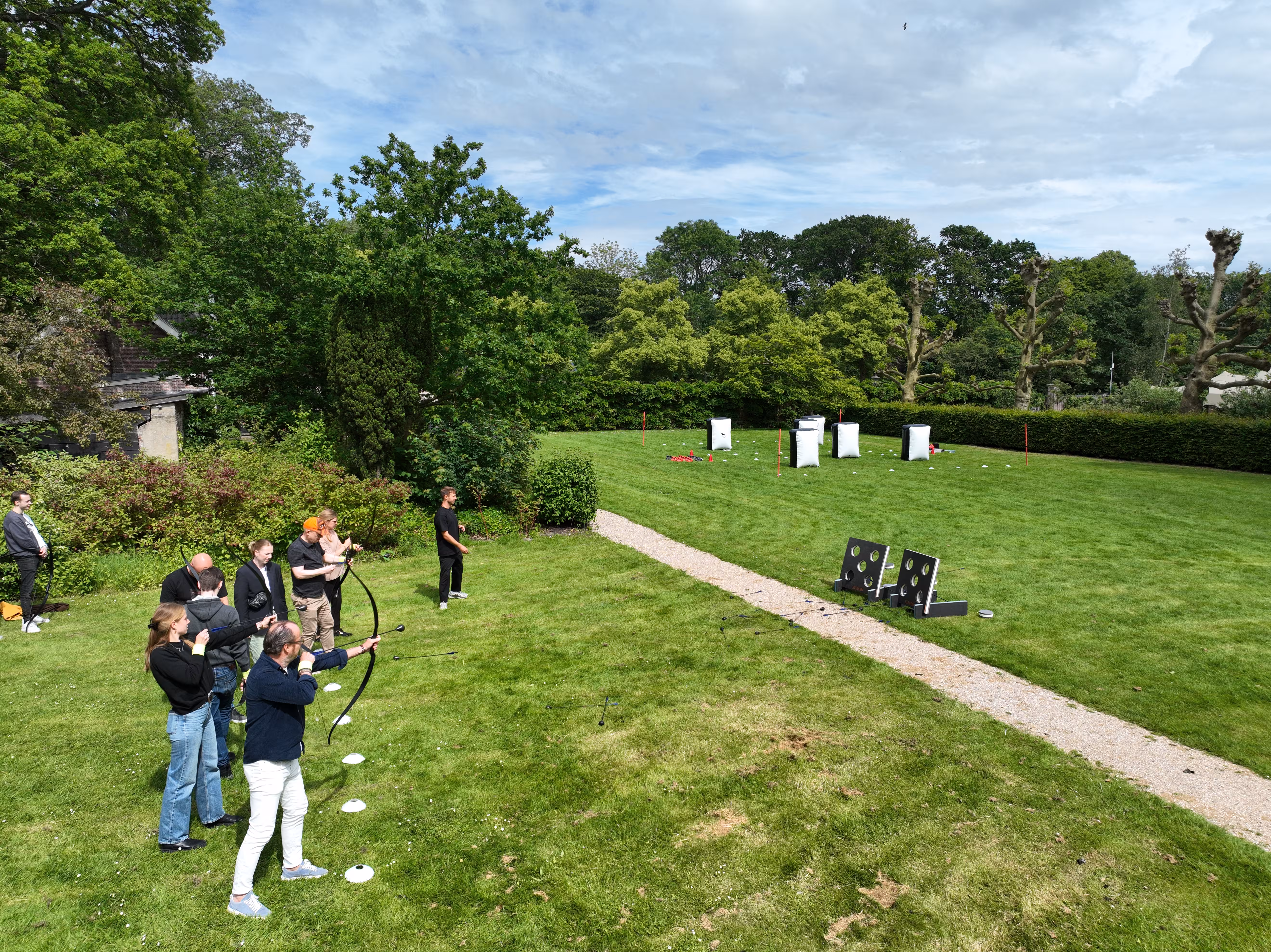 De deelnemers staan achter witte pionnen en schieten op een target met pijl en boog