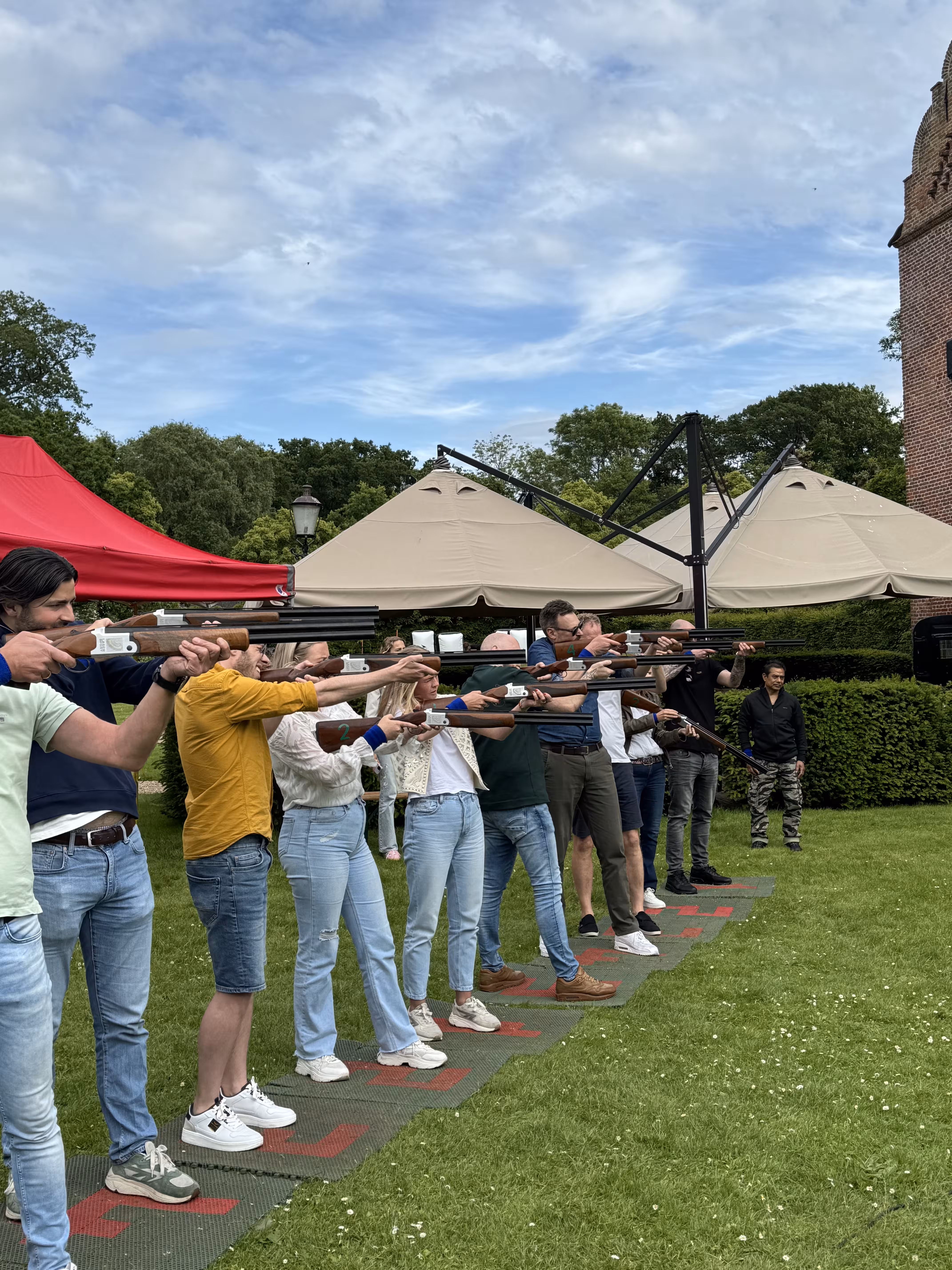 De groep staat op een rij met een geweer in de hand en richting op een laser kleiduif