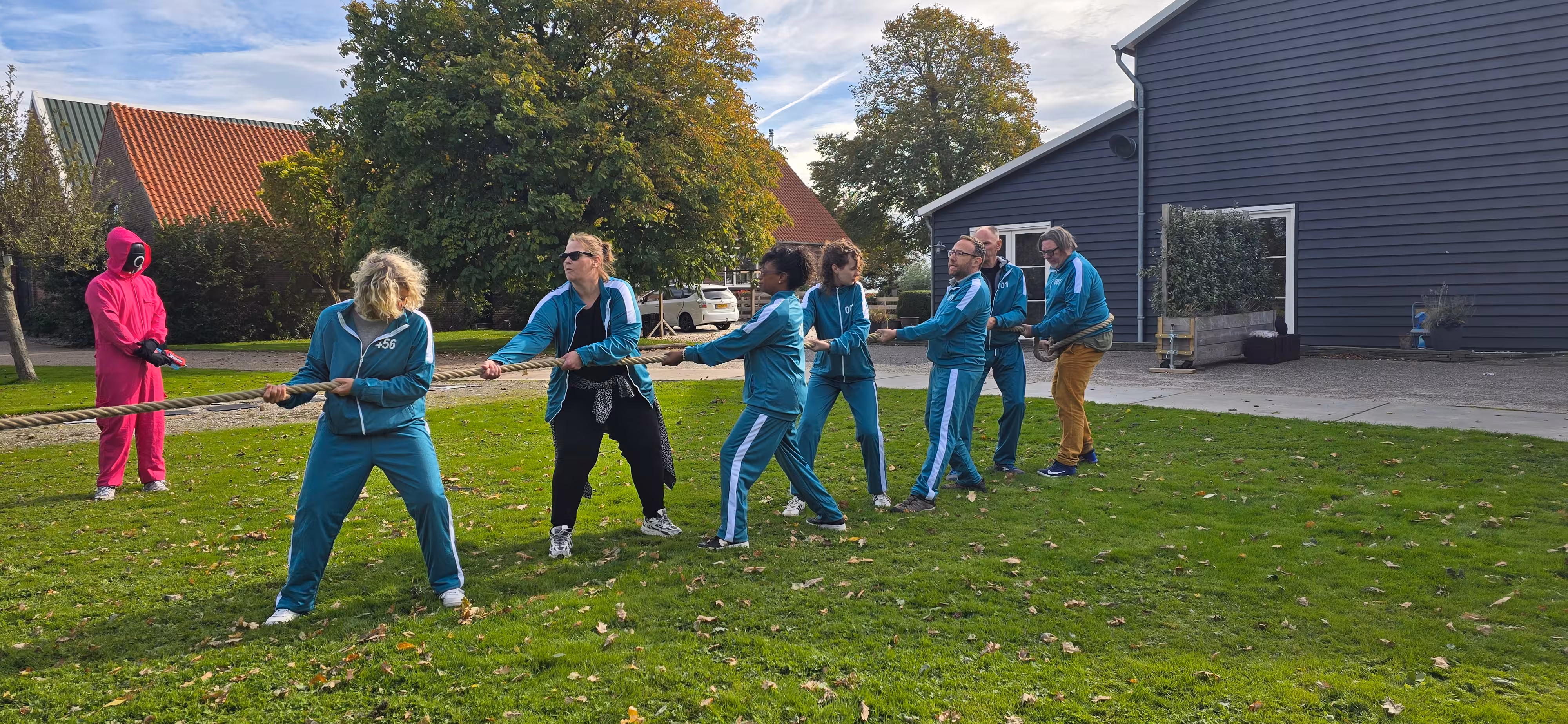 Het team dat in het blauw gekleed is neemt deel aan het onderdeel touwtrekken tijdens de workshop squid game