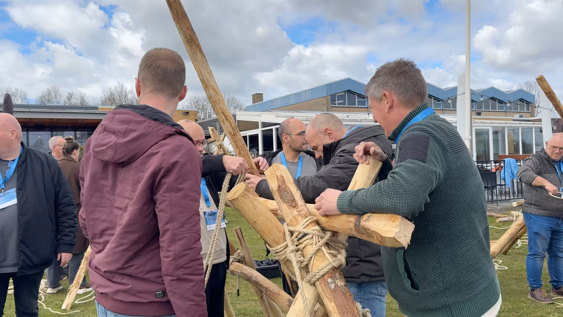 De houten balken worden met touw aan elkaar bevestigd door een deelnemend team