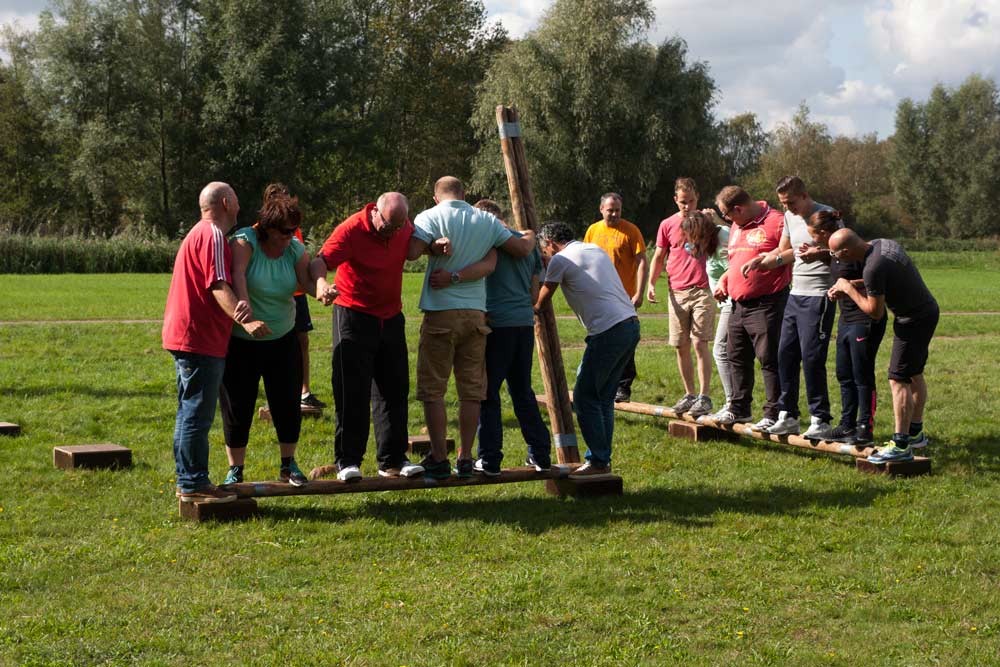 Twee groepen mensen strijden tegen elkaar in een teambattle waarbij ze op planken staan op een grasveld