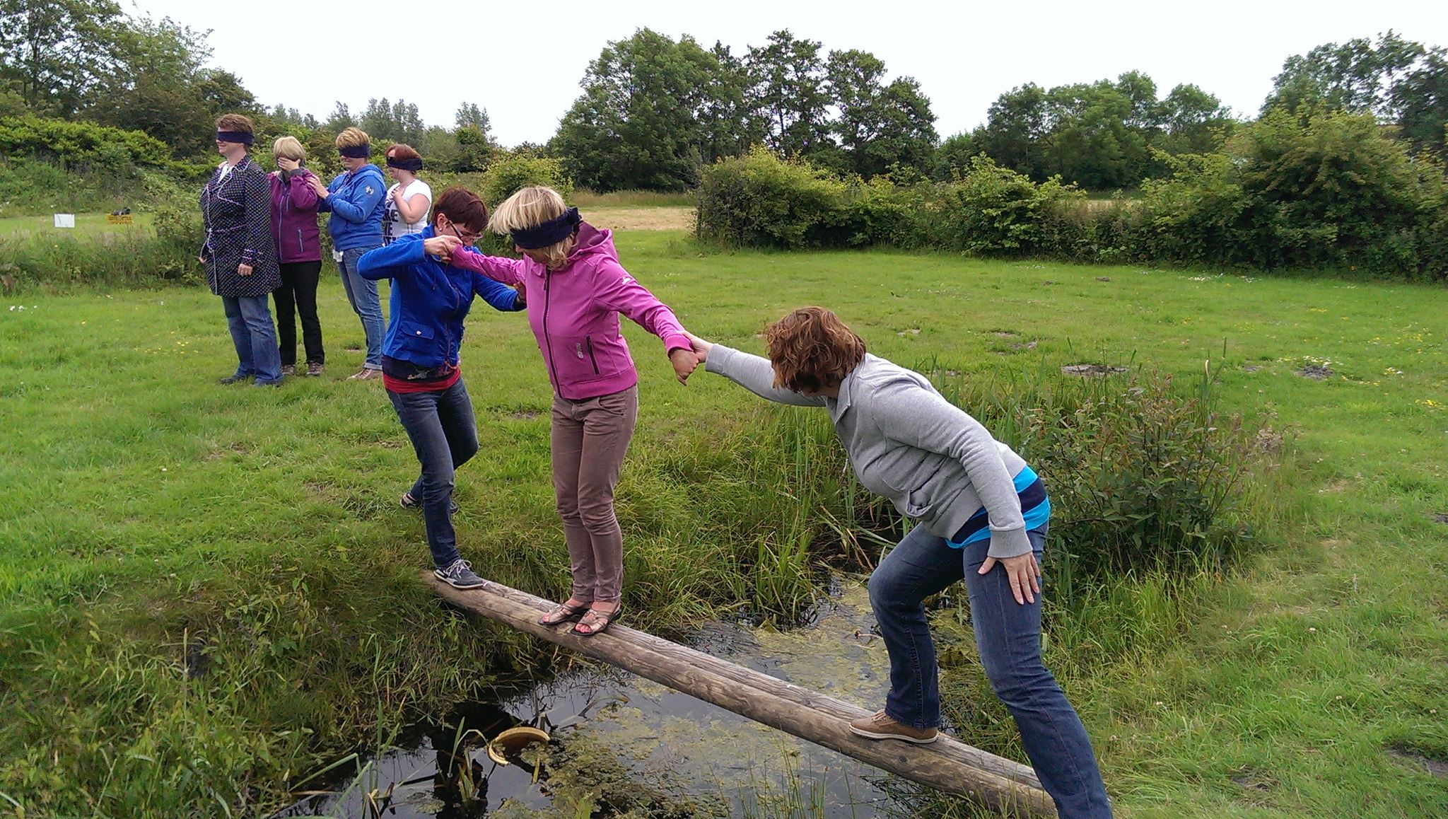 Mensen helpen elkaar terwijl ze geblinddoekt over een sloot lopen tijdens Alleskunner Teambuilding door BuitenEvents