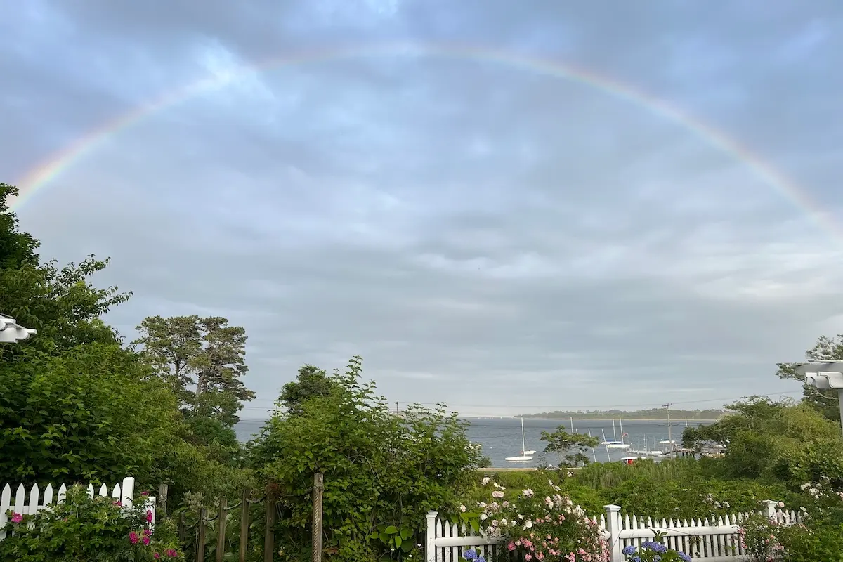 A double rainbow arches over Pleasant Bay in Orleans MA. The sky is cloudy with blue breaking through.