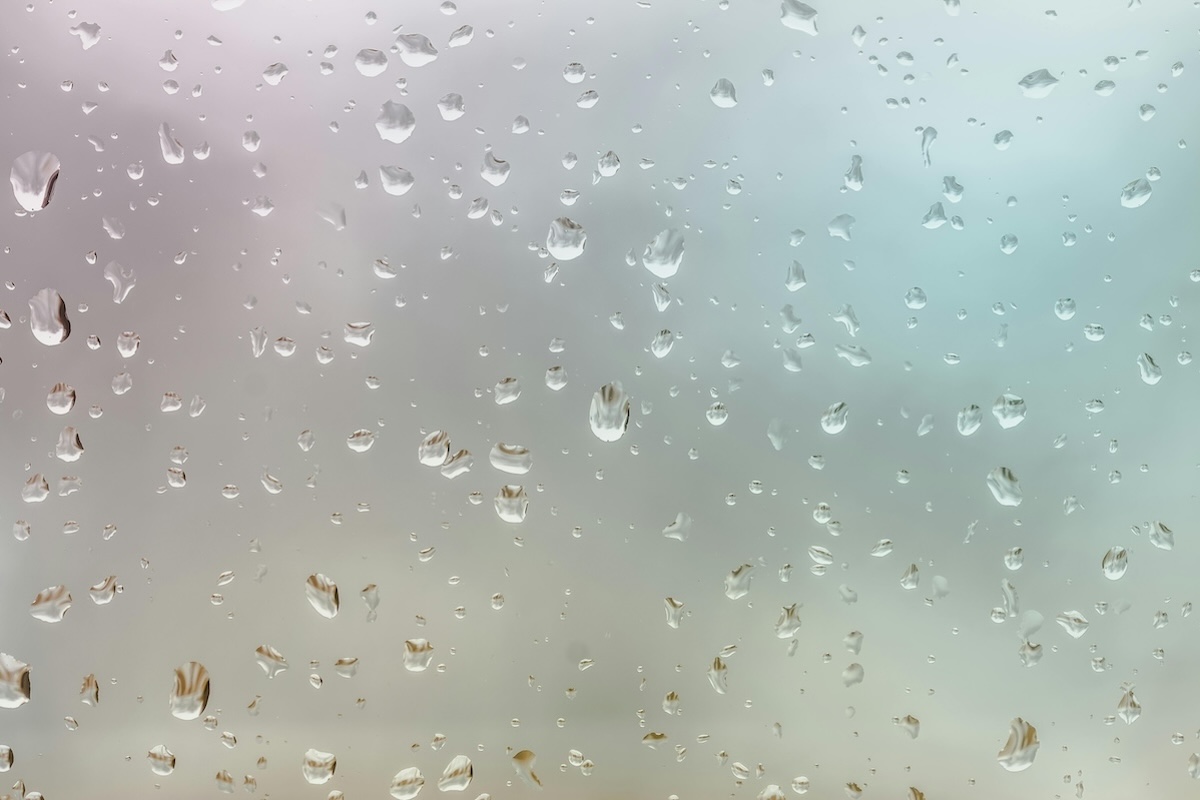 Close up of rain drops on a glass pane. Outside the day is gray.