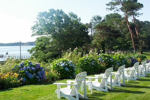 The front yard at A Little Inn on Pleasant Bay with adirondack chairs on a sunny day in the summer.