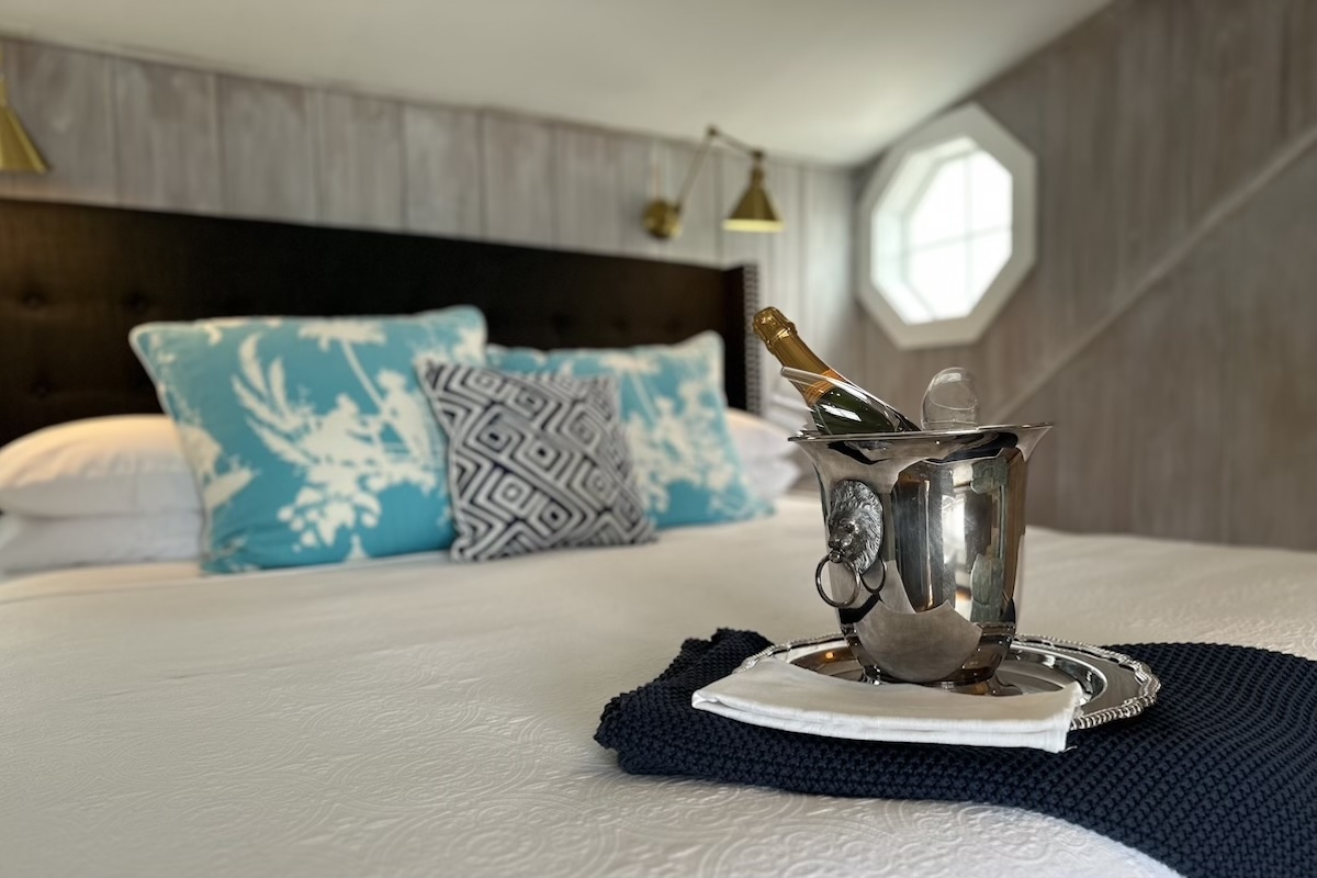 A bottle of champagne in a silver holder sits on a made bed in one of the guest rooms at A Little Inn on Pleasant Bay.